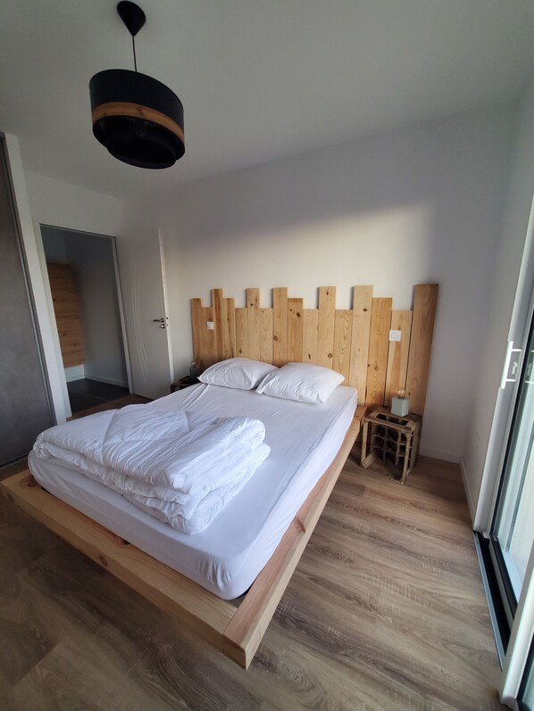 Un dormitorio moderno con estructura de cama de madera, ropa de cama blanca y cabecero de madera.