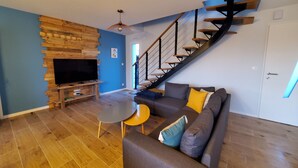 Ein Wohnzimmer mit Fernseher, Holzwand, Treppe und einer Couch mit Kissen.