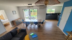 Ein modernes Wohnzimmer mit Sofa, Couchtisch, Esstisch mit Stühlen und einer Küchenzeile.