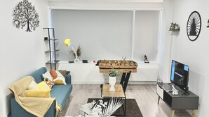 Ein modernes Wohnzimmer mit Sofa, Couchtisch, Esstisch für vier Personen und einem Fernseher auf einem Schrank.