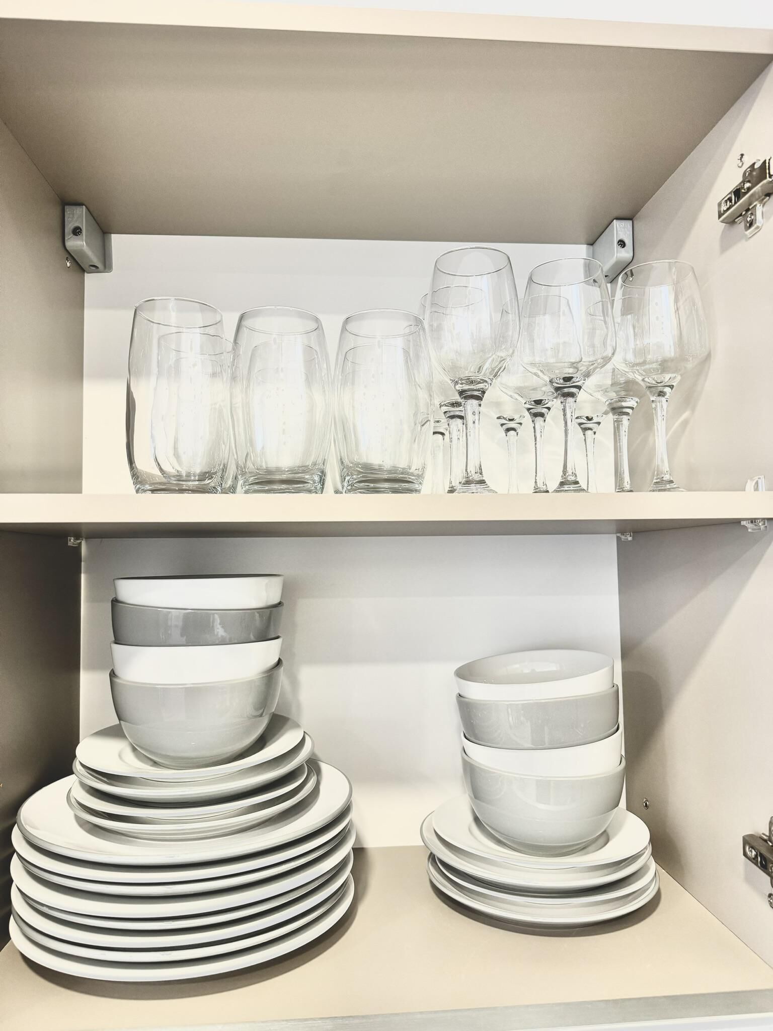 A storage area with shelves holding clear wine glasses and stacked white plates.