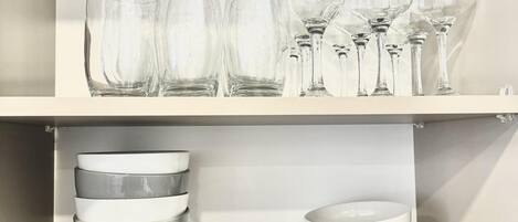 A storage area with shelves holding clear wine glasses and stacked white plates.