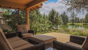 A covered outdoor seating area with wicker furniture and a view of a lake and trees.