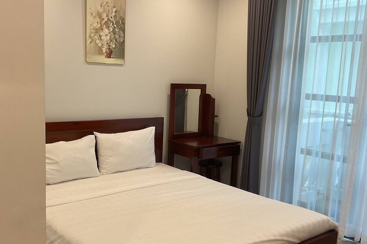 A hotel room with a large bed, a desk, a chair, a mirror, and a window with curtains.