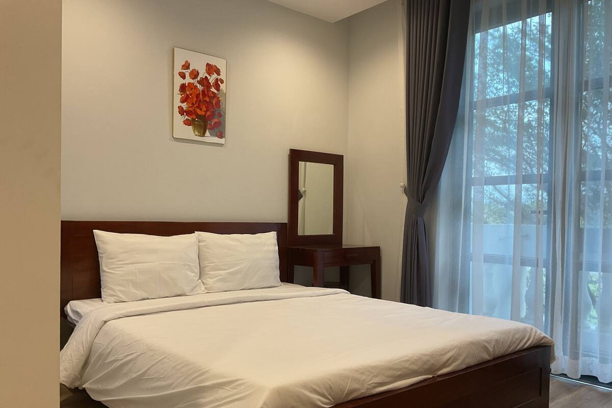 A neatly made bed in a hotel room with a wooden headboard, a small bedside table, and a mirror.