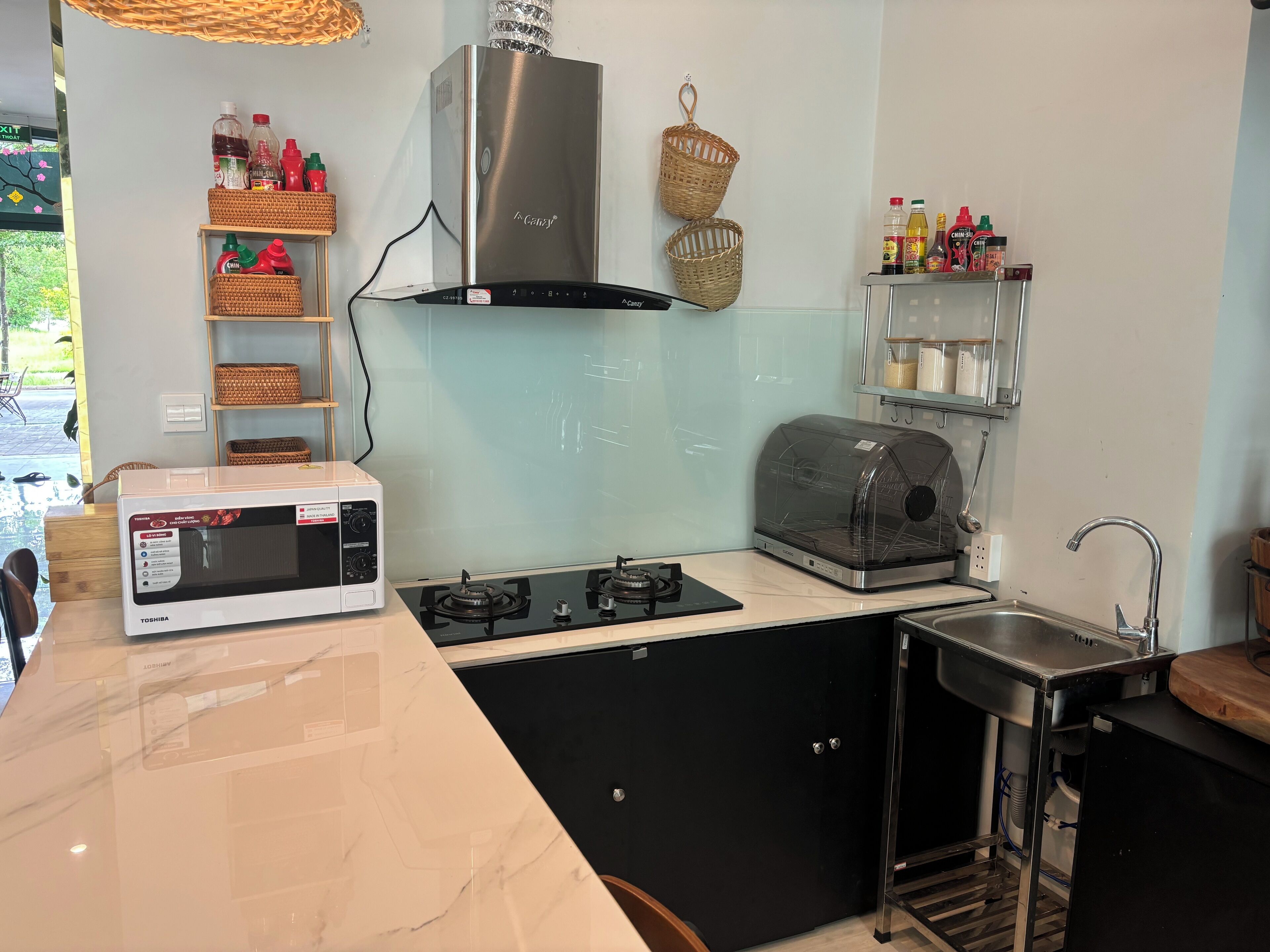 A modern kitchen with a microwave, stove, and toaster. There are baskets and condiment bottles on shelves.