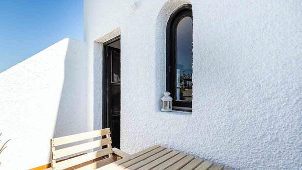 Un edificio bianco con una panchina di legno all'esterno, una porta nera e una finestra con una lanterna.