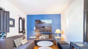 Un soggiorno con divano, due tavolini rotondi, camino e un grande quadro raffigurante una scena costiera.