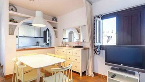Un ambiente compatto con angolo cottura, zona pranzo con tavolo e sedie, e televisione su un mobile.