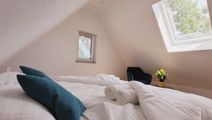 A bedroom with a sloped ceiling, a small window, a chair, and a potted plant. - The modern, newly renovated  90-square-meter apartment is waiting for you (Friedrichshafen)