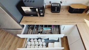 A kitchen with a microwave, toaster, and wooden countertop. There is a drawer with utensils and cups. - The modern, newly renovated  90-square-meter apartment is waiting for you (Friedrichshafen)
