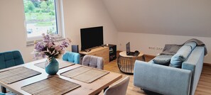 Un salon moderne avec une table à manger, des chaises bleues, un canapé et un téléviseur.