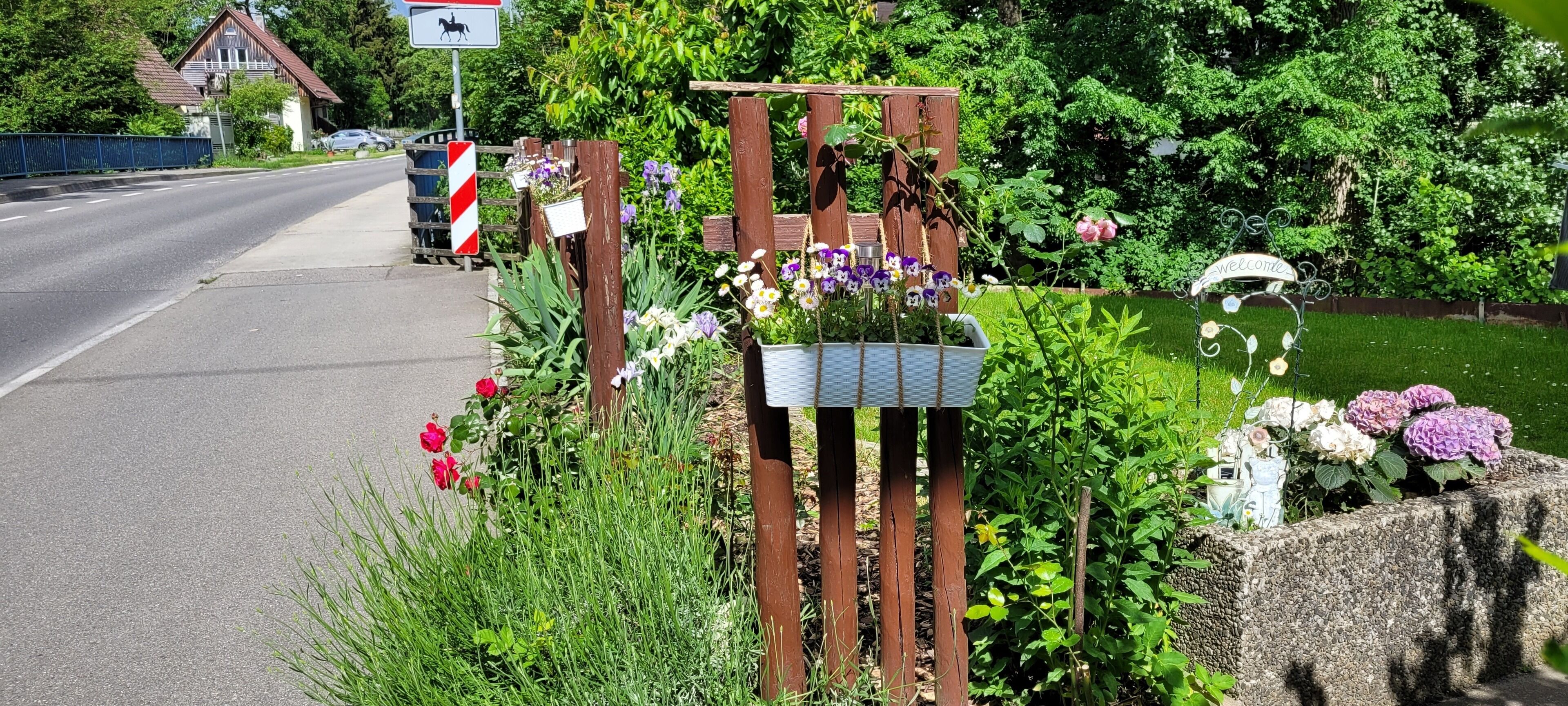 A rural road with a wooden gate, a welcome sign, and a mailbox.