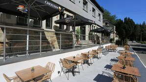 An outdoor cafe with wicker tables and chairs, umbrellas, and a stone building in the background. - Hôtel L'ermitage (Houffalize)