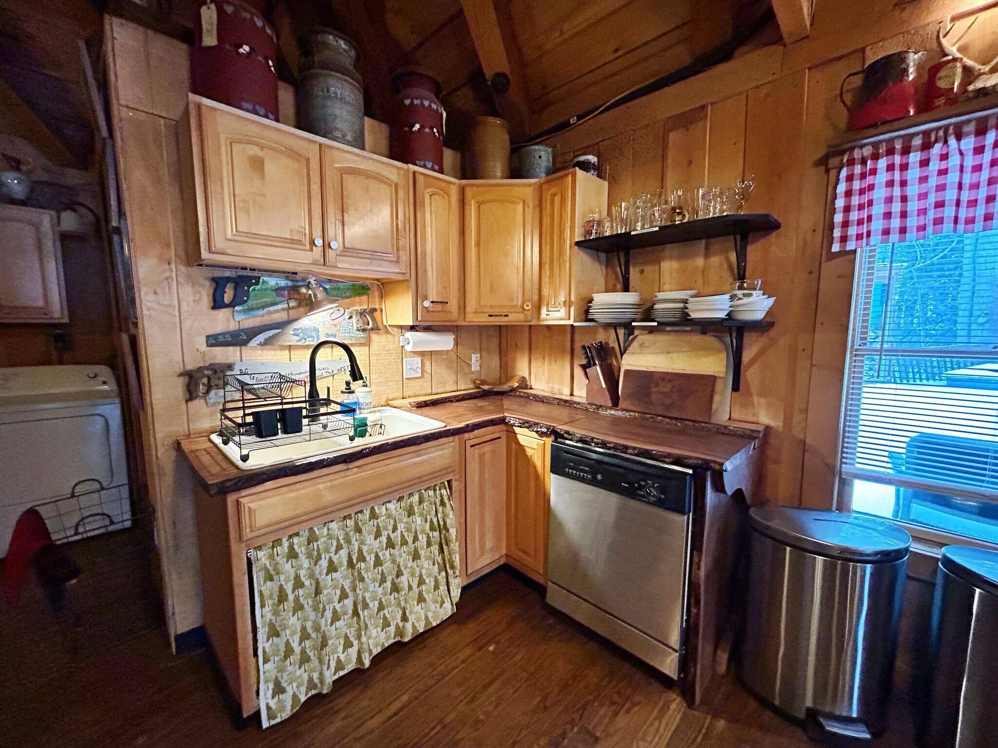Una cocina compacta con armarios de madera, lavavajillas integrado y una ventana con persianas.
