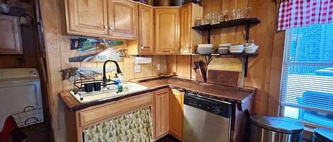 Una cocina compacta con armarios de madera, lavavajillas integrado y una ventana con persianas.