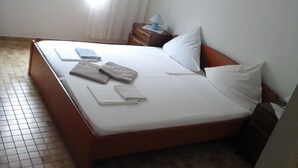Habitación individual con una cama de madera, ropa de cama blanca y una mesita de noche con lámpara.