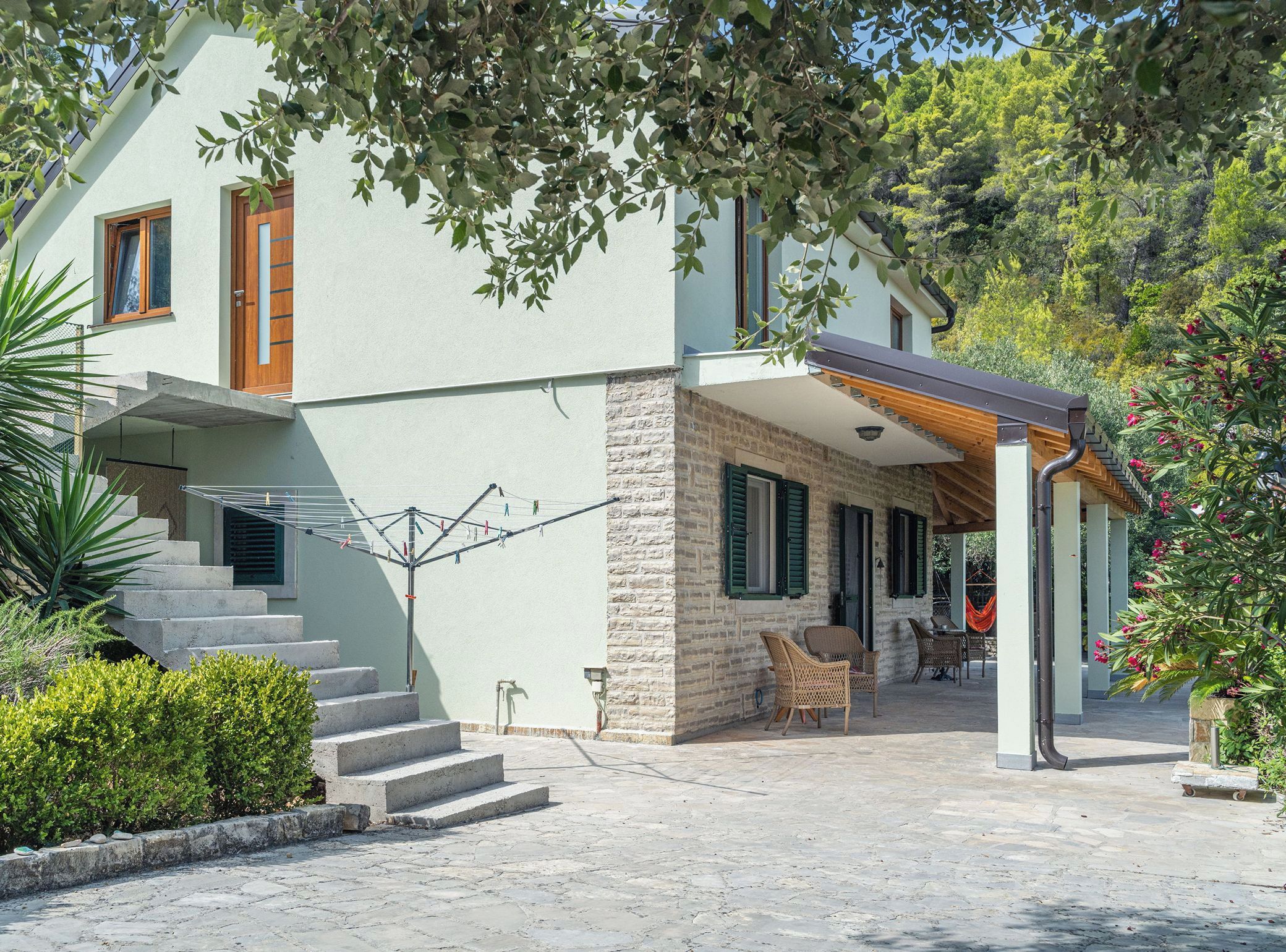 A two-story house with a stone facade, a wooden door, and a balcony with wicker furniture.