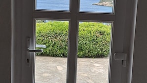 A door with multiple windows, each offering a view of a stone patio, a green hedge, and the ocean. - Vacation House Marija, Korčula (Korcula)