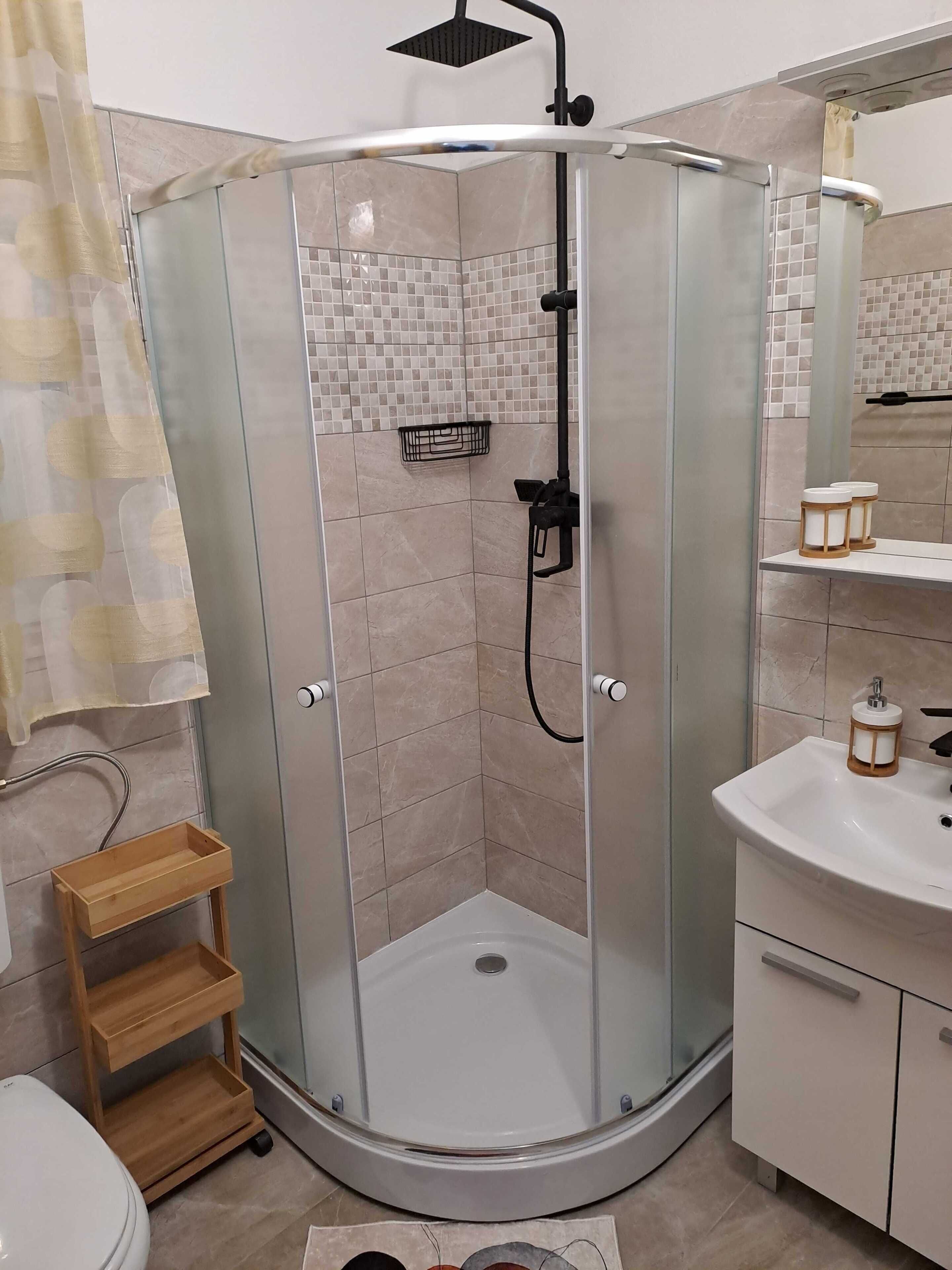 A modern bathroom with a glass-enclosed shower, a white sink, and a wooden shelf.
