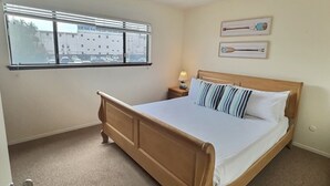 A bedroom with a wooden bed, a window with blinds, a nightstand with a lamp, and two wall-mounted paintings. - Pismo Shores Paradise #111 - beach access - Pet Ok (Pismo Beach)