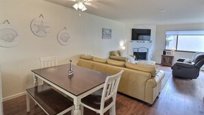 A dining area with a wooden table and chairs, a beige sofa, and a ceiling fan. - Pismo Shores Paradise #111 - beach access - Pet Ok (Pismo Beach)