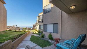 A residential building with a small patio area, a view of the ocean, and a clear sky. - Pismo Shores Paradise #111 - beach access - Pet Ok (Pismo Beach)