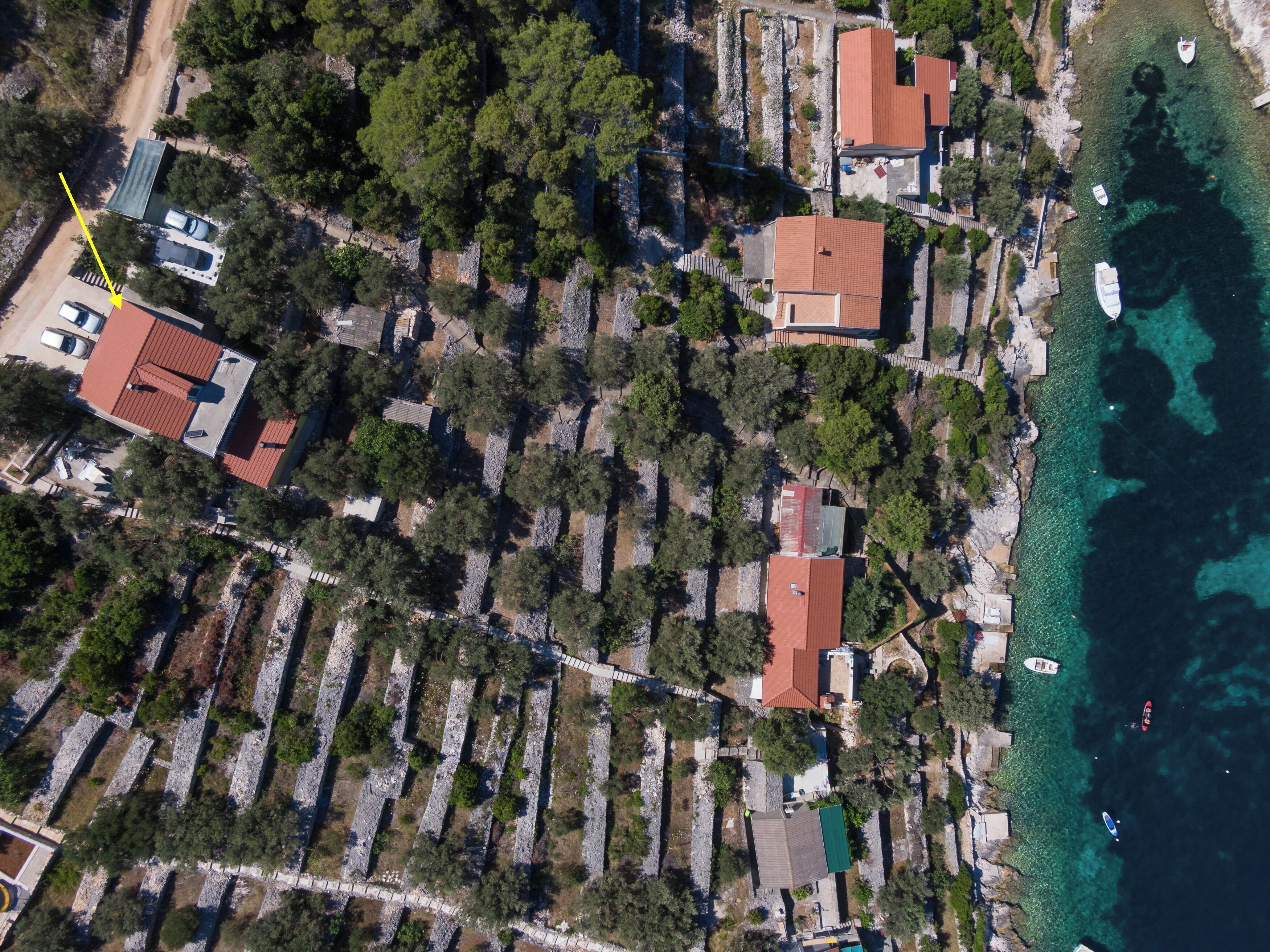 An aerial view of a coastal area with terraced houses, clear blue waters, and boats.