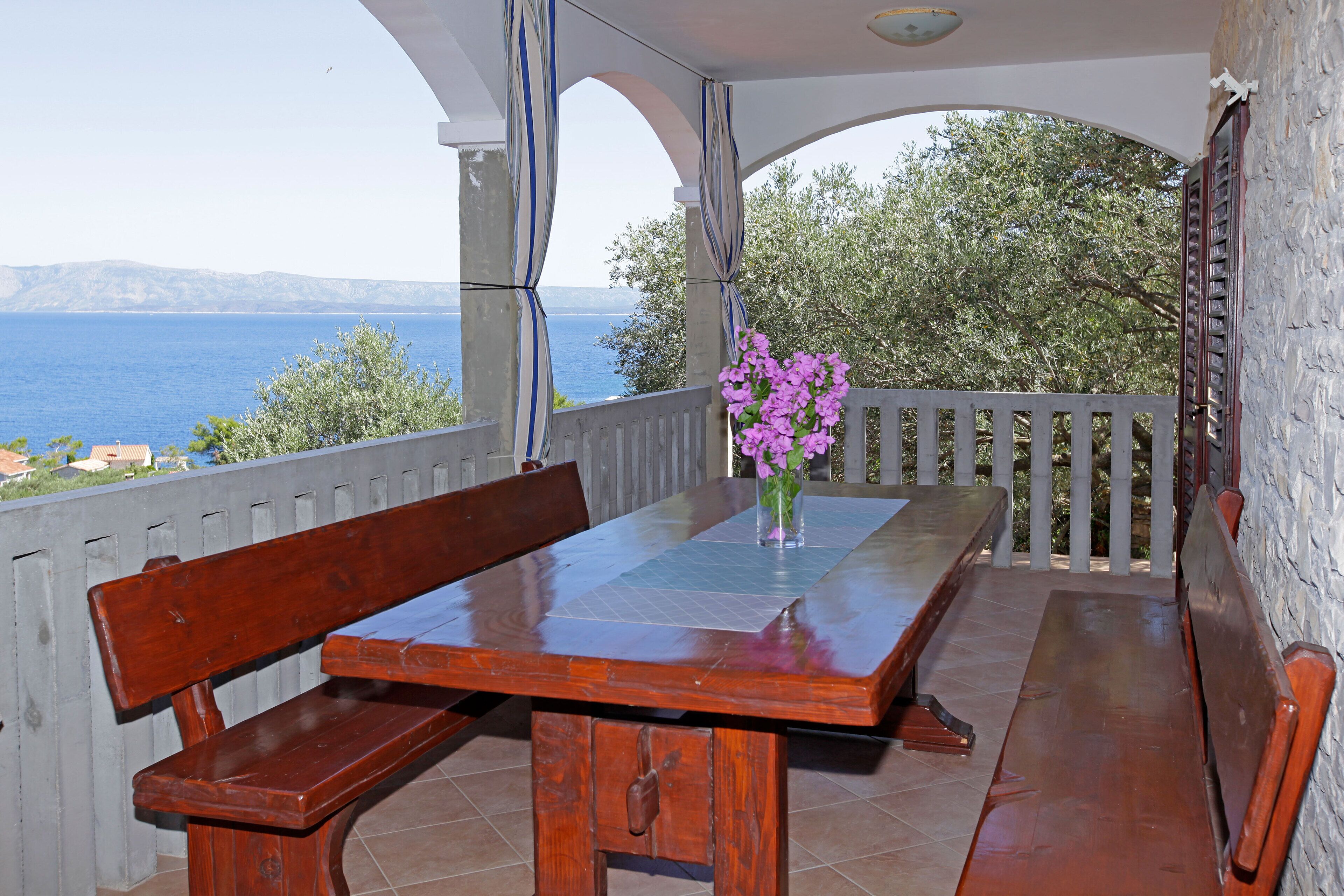 A wooden table with benches on a balcony overlooking a body of water.