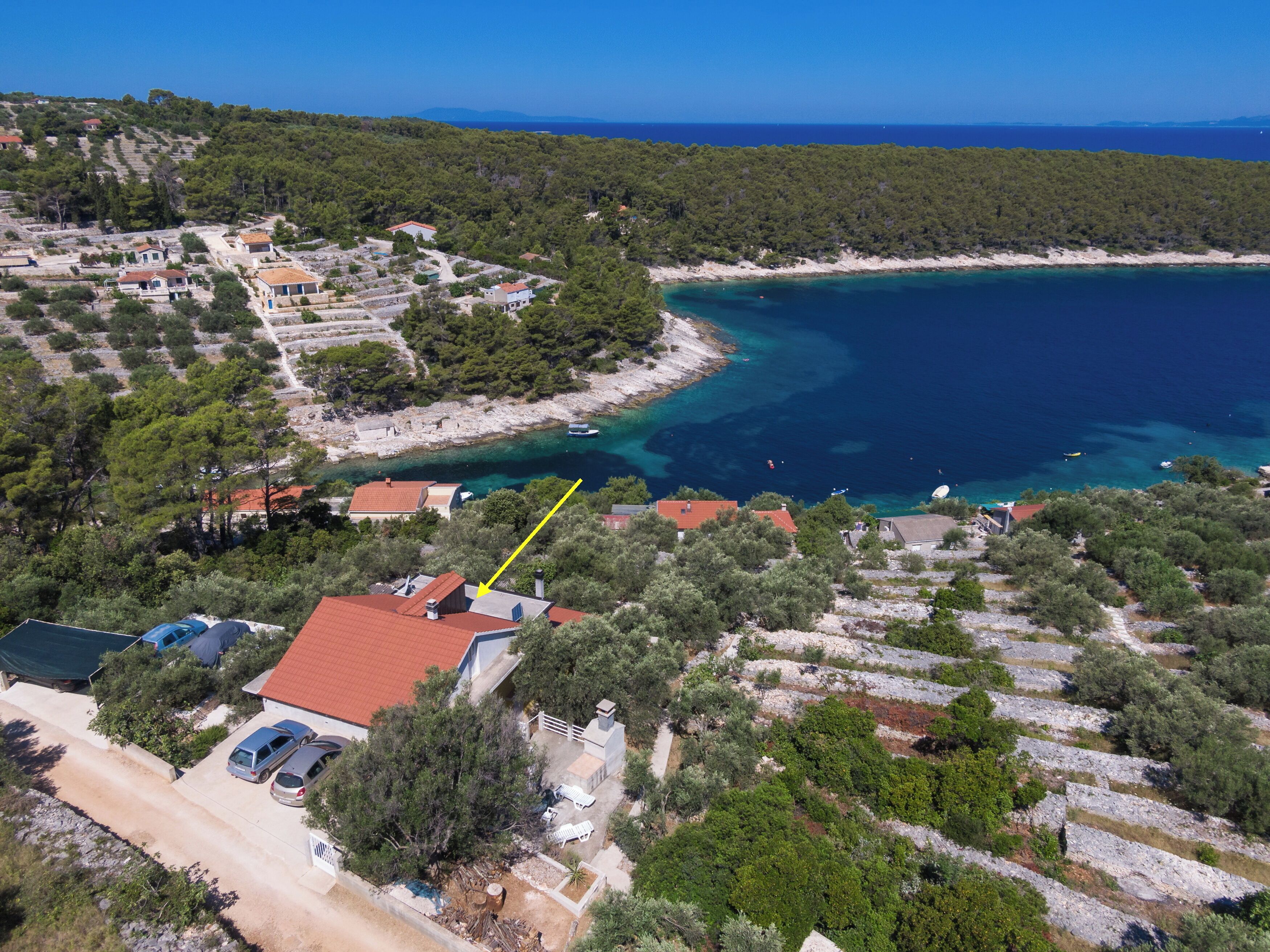 An aerial view of a coastal area with a mix of residential buildings and natural landscape, including a clear view of the sea and a marked property.