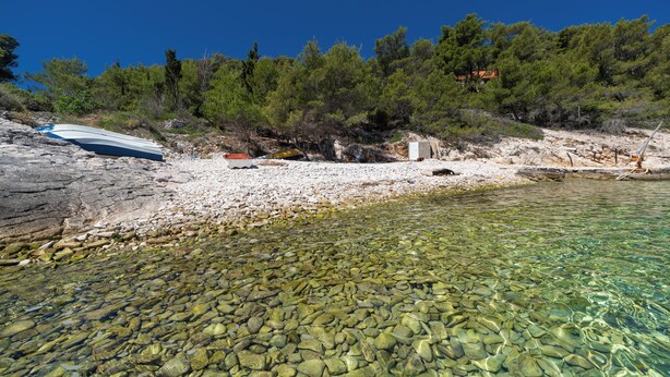 Une plage rocheuse aux eaux cristallines, un bateau et une colline boisée.