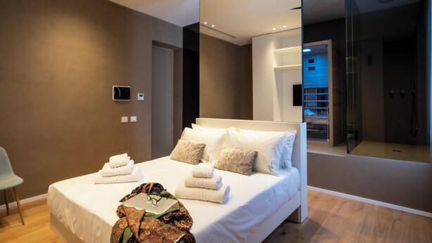 A modern hotel room with a large bed, a glass shower enclosure, and a view of the city. - Amorgiù Luxury Room (Palermo)