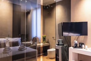 Une chambre d’hôtel moderne équip ée d’un lit, d’une coiffeuse avec un miroir, d’un lavabo, de toilettes et d’un téléviseur fixé au mur.