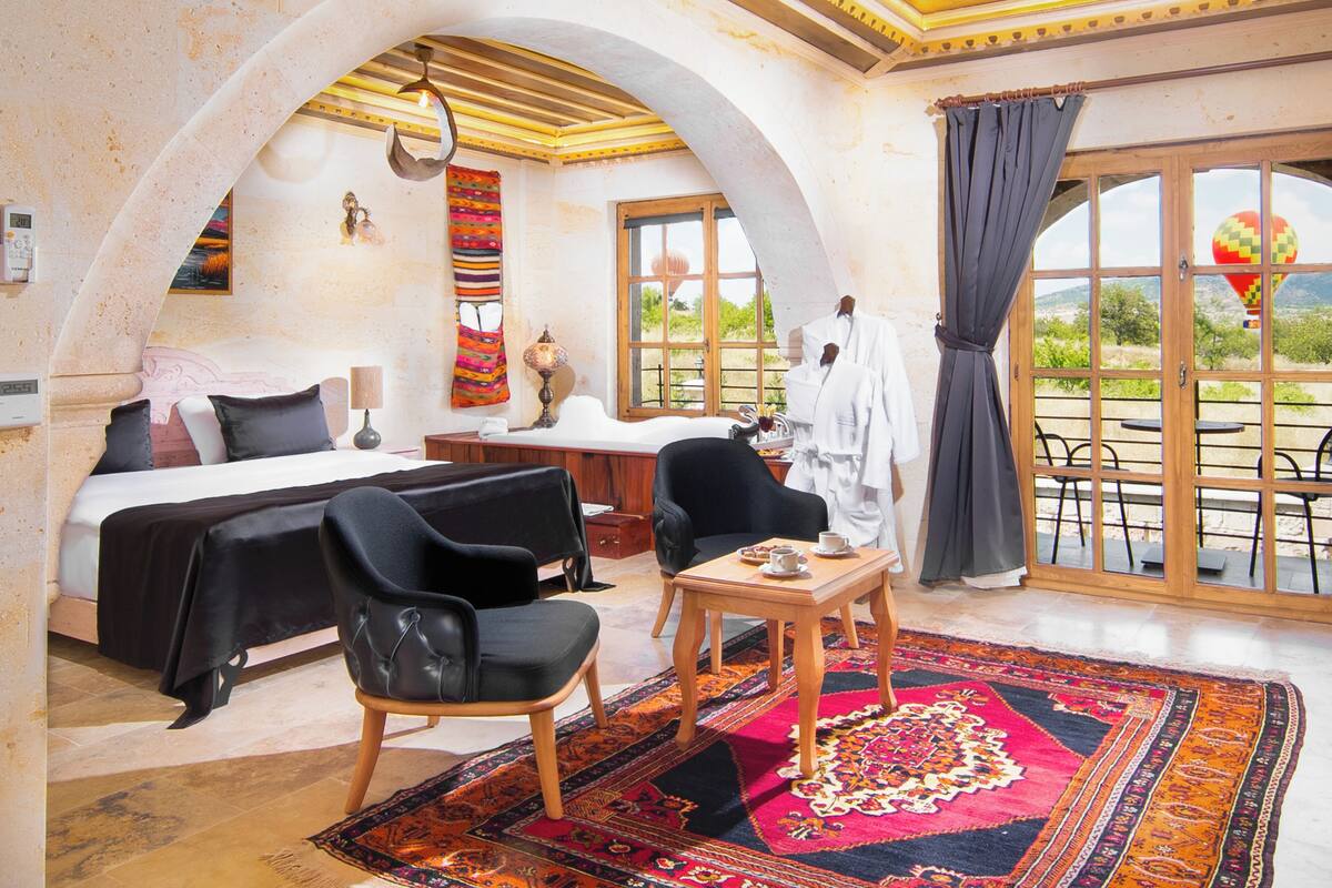 A hotel room with a bed, two chairs, a small table, a window with curtains, and a view of the outdoors.