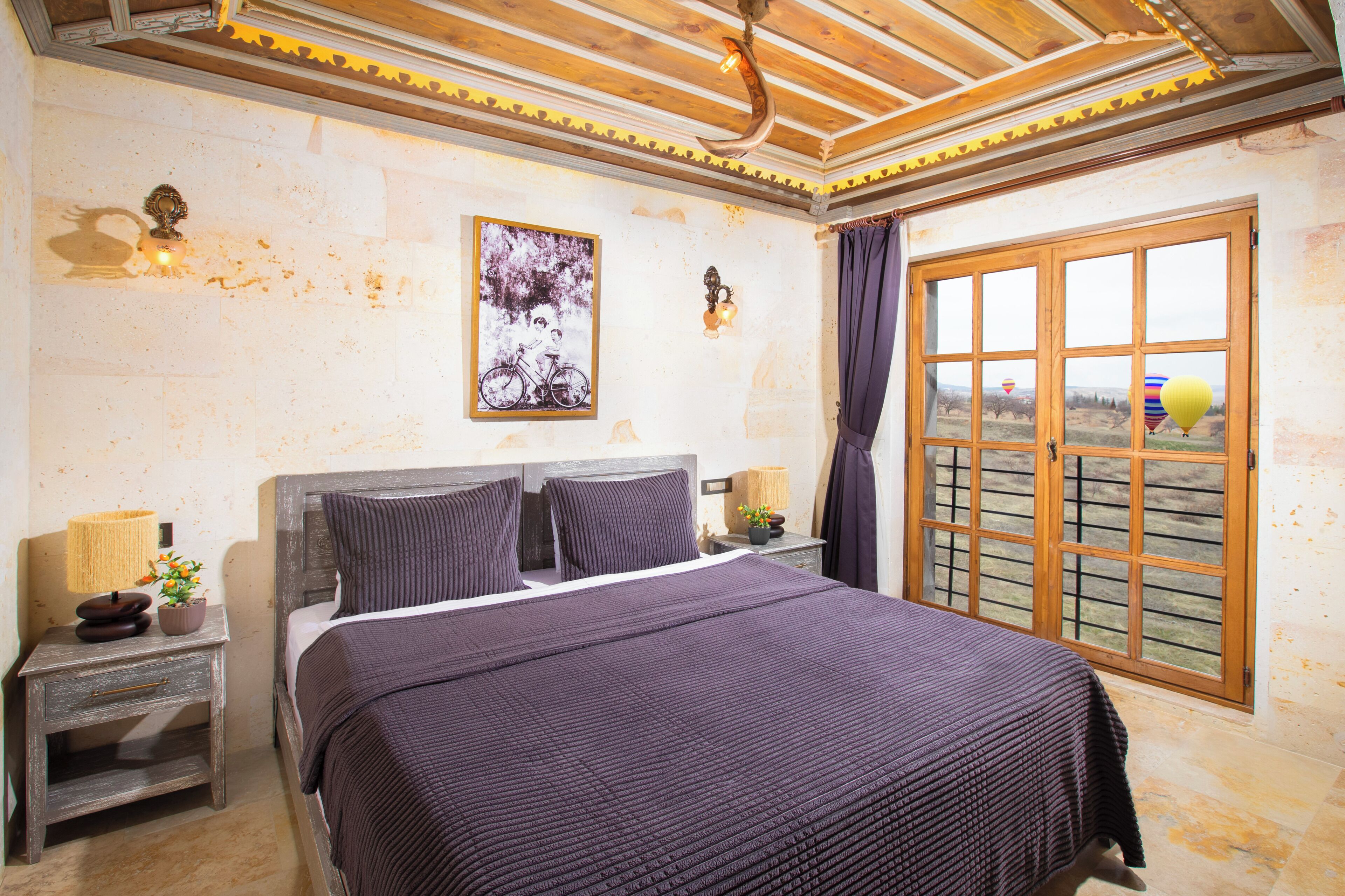 A bedroom with a large bed, a nightstand with a lamp, a window with curtains, and a wall-mounted picture.