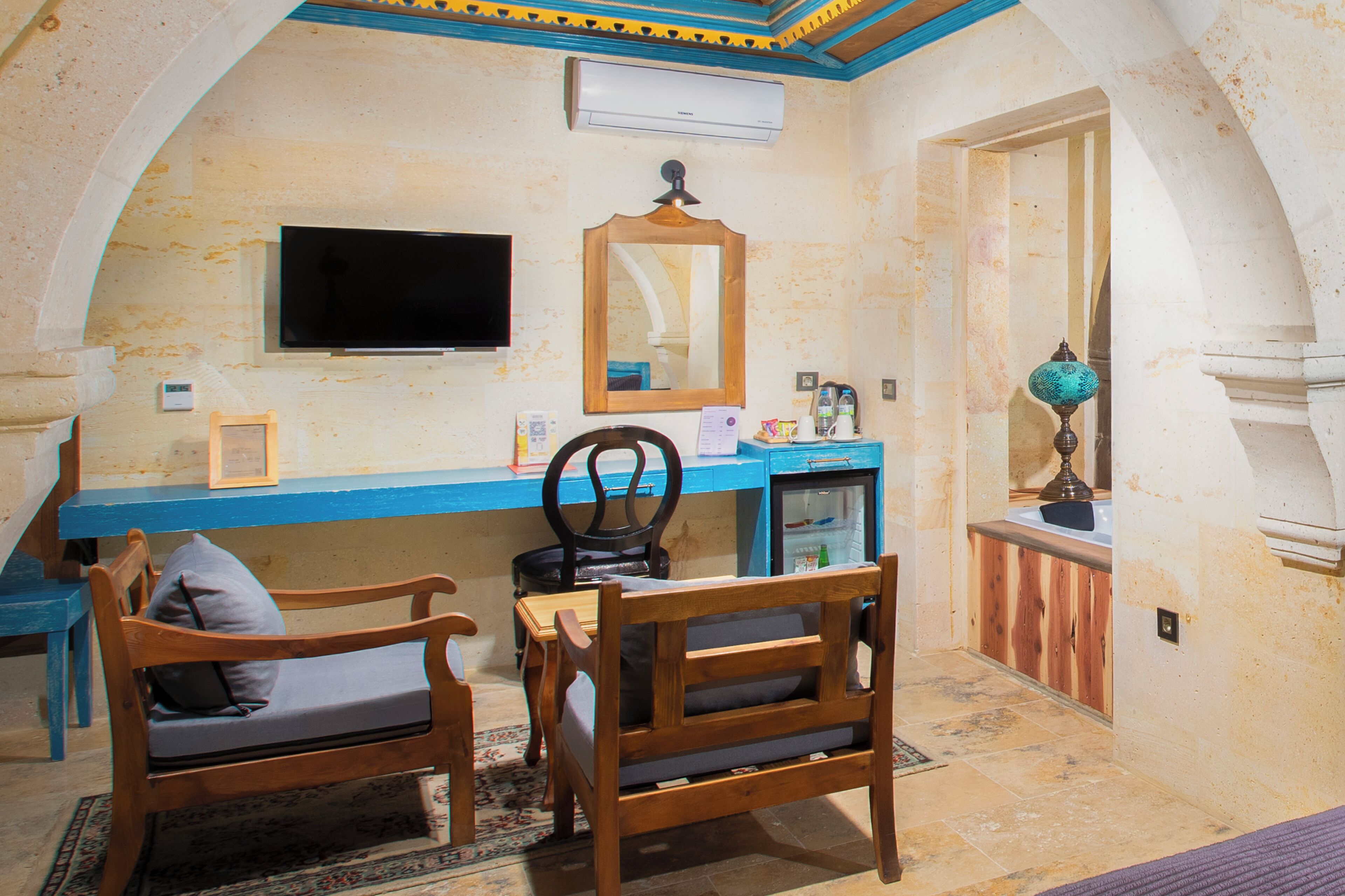 A room with a wooden desk, two chairs, a television, a mirror, and a small refrigerator.