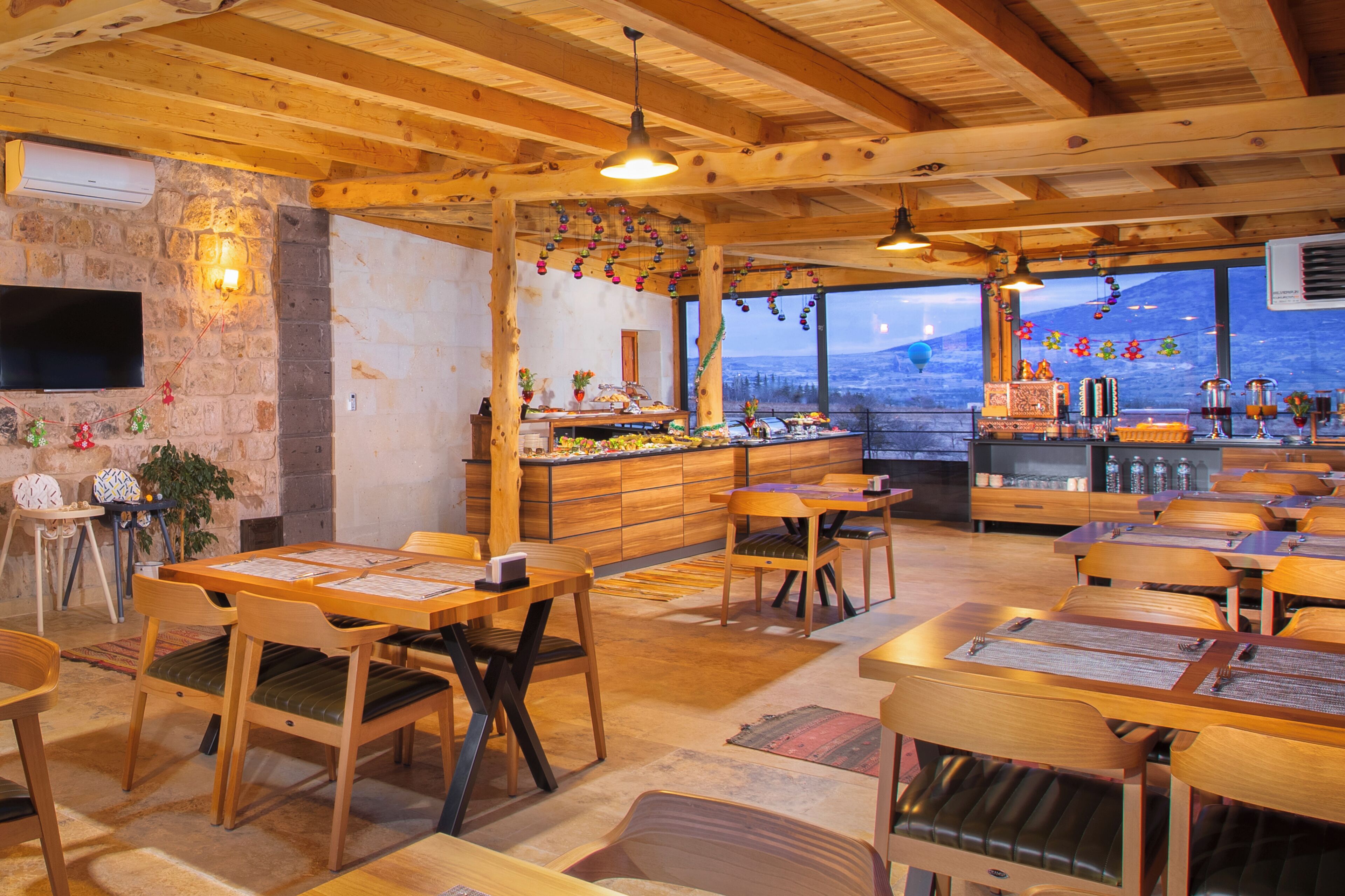 A restaurant with wooden tables and chairs, a stone wall, and a view of a mountain.