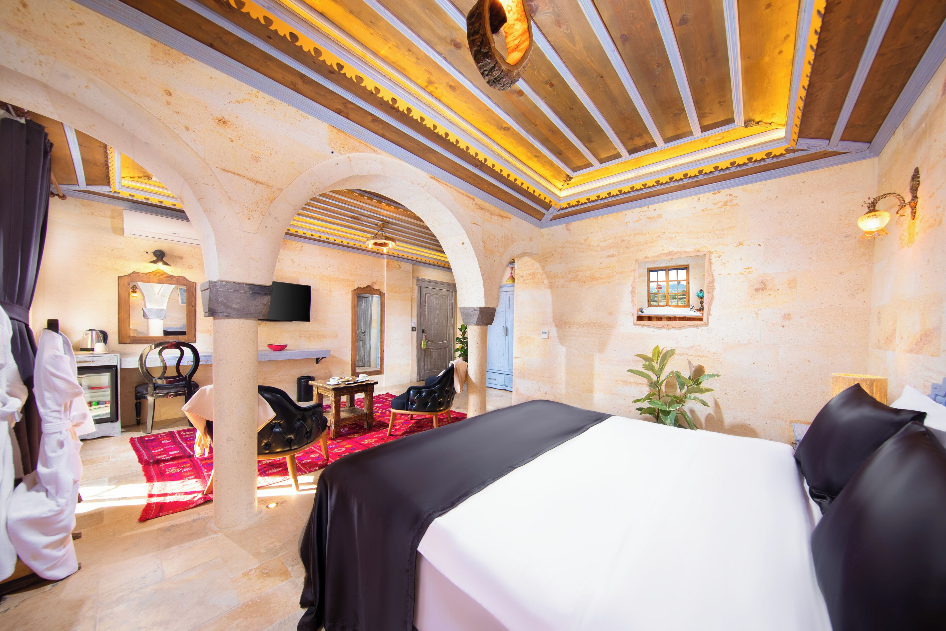 A hotel room with a large bed, a desk with a chair, a mirror, a small table, and a red rug.