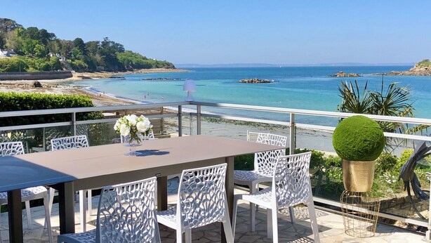 A terrace with a table and chairs, overlooking a beach and the sea.