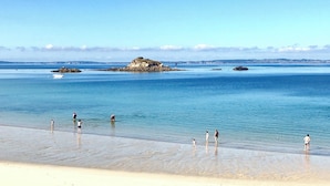 A beach with clear water, a rocky outcrop, and people in the water.