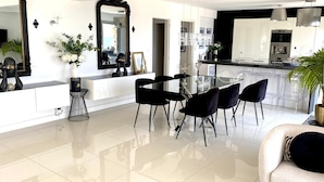 A modern kitchen with a dining area, featuring a glass table and black chairs, a large mirror, and a potted plant.