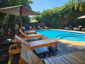 A swimming pool with wooden loungers and umbrellas, surrounded by greenery. - HOTEL BL (Puerto Iguazú)