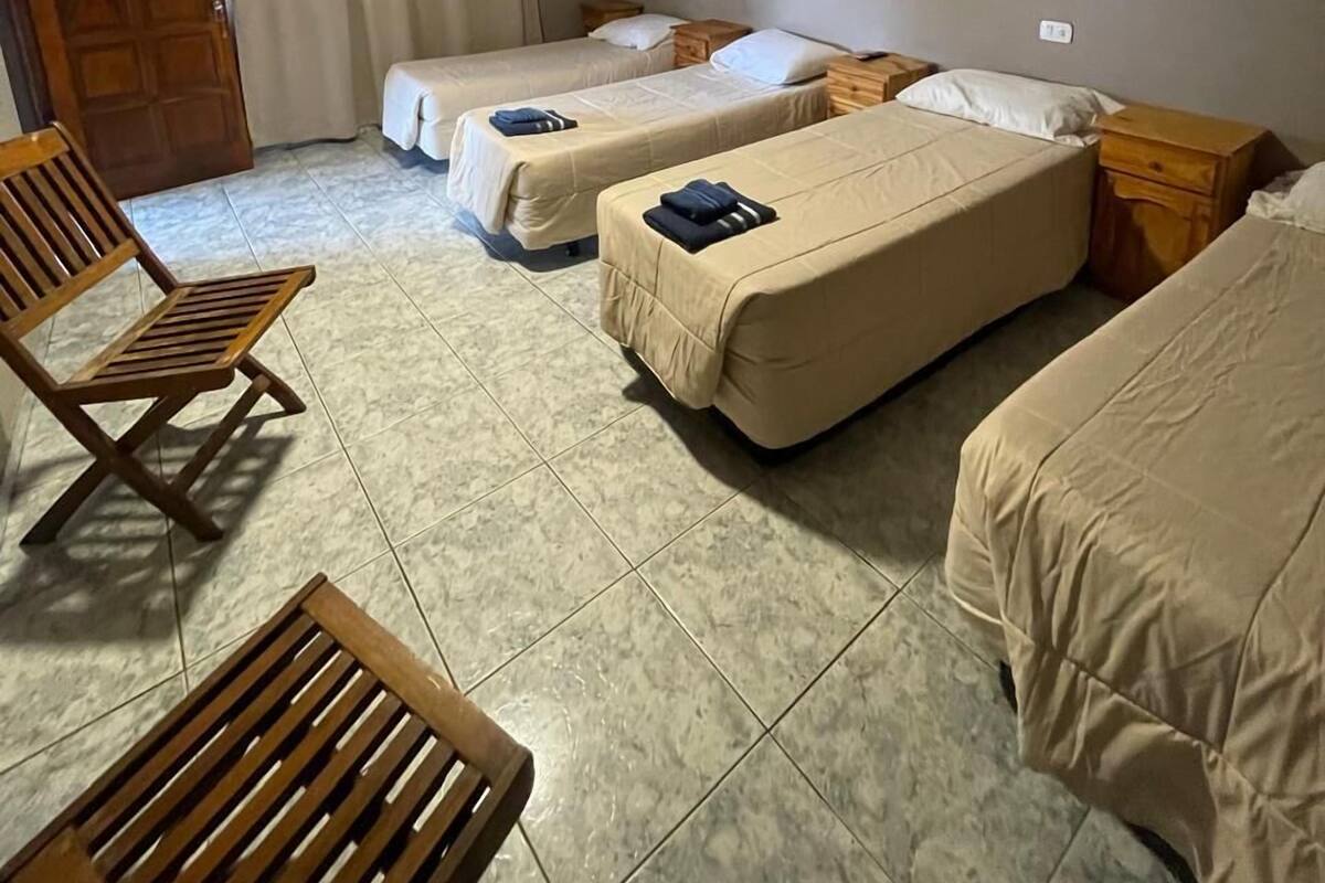 A room with three beds, a wooden chair, and a small table.