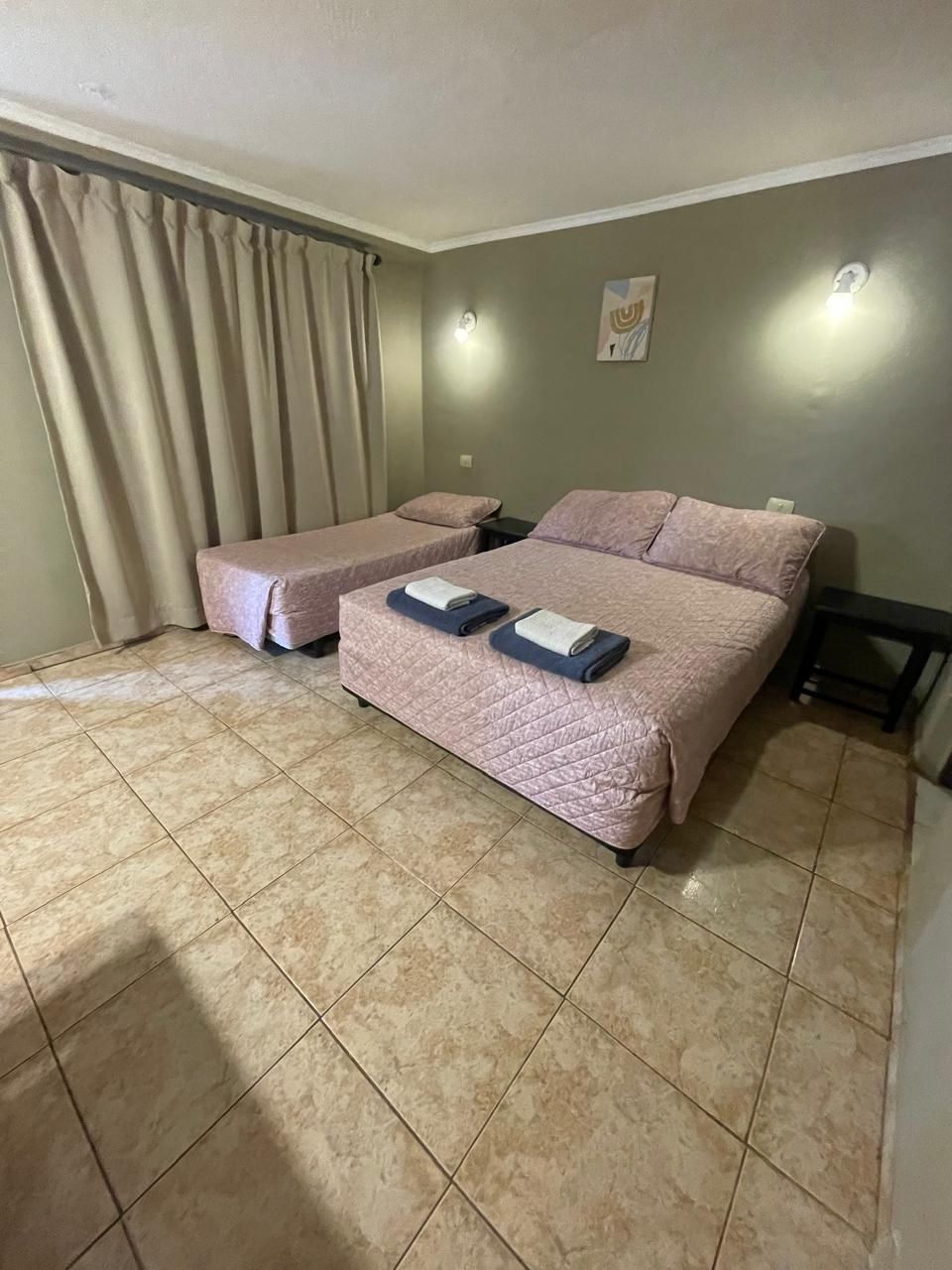 A hotel room with a bed, a bedside table, a chair, and a curtain.
