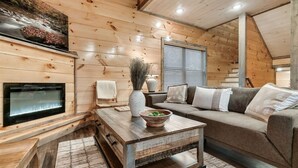 A cozy cabin interior with a fireplace, wooden walls, a sofa, and a coffee table. - Near Dollywood | Hot Tub, Game Room & Home Theater (Sevierville)