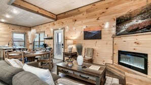 A cozy cabin interior with a wooden interior, a dining area, a fireplace, and a television mounted on the wall. - Near Dollywood | Hot Tub, Game Room & Home Theater (Sevierville)
