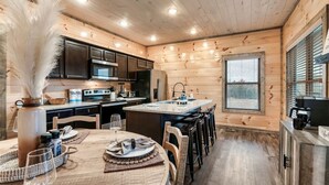 A cozy kitchen with wooden walls, a central island, and a dining area with chairs and a table set for two. - Near Dollywood | Hot Tub, Game Room & Home Theater (Sevierville)