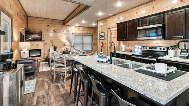 A modern kitchen with wooden paneling, granite countertops, and stainless steel appliances. - Near Dollywood | Hot Tub, Game Room & Home Theater (Sevierville)