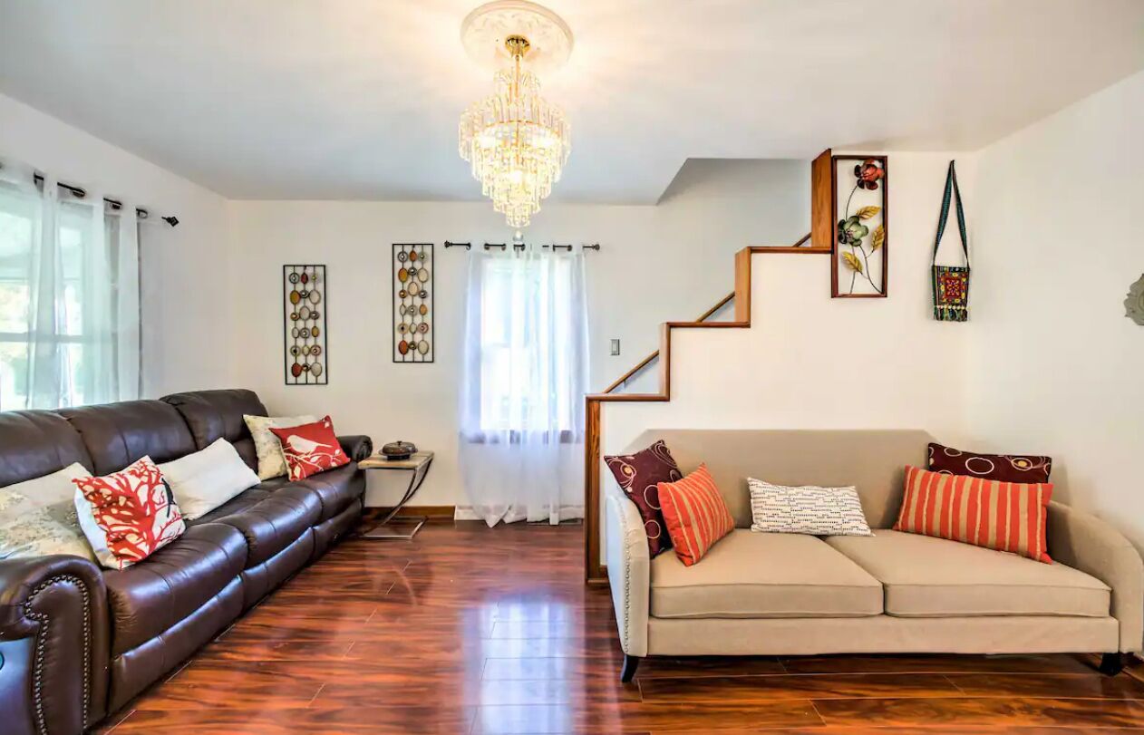 A living room with a dark brown leather sofa, a beige sofa, a chandelier, and a staircase.