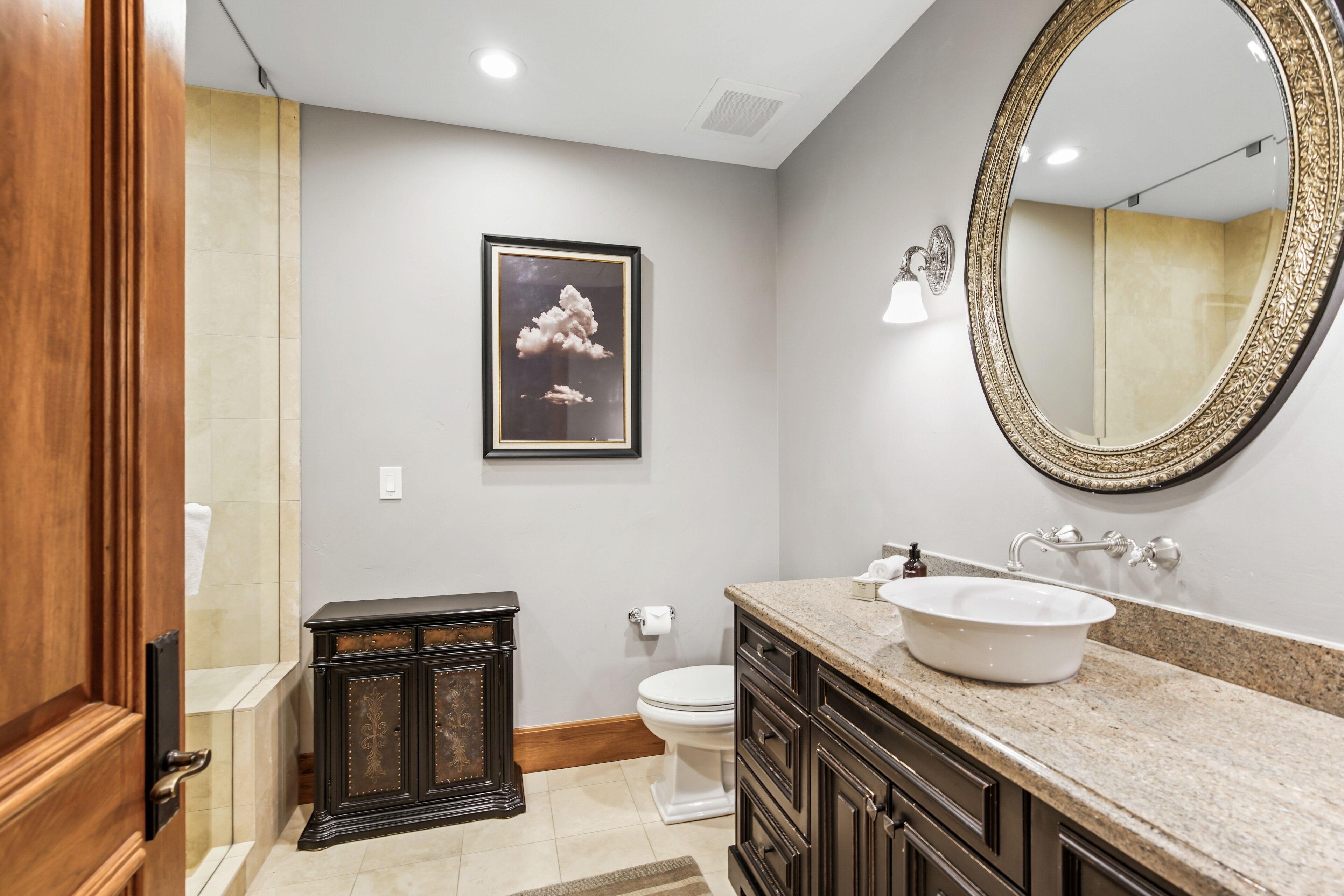 A bathroom with a vanity, sink, mirror, toilet, and framed artwork on the wall.